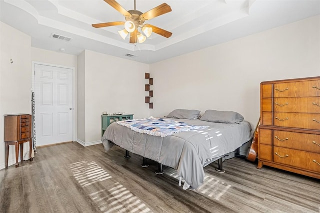 bedroom with wood finished floors, visible vents, and a raised ceiling