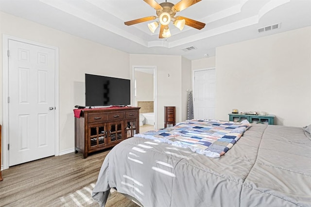 bedroom with ensuite bath, a ceiling fan, a tray ceiling, and visible vents