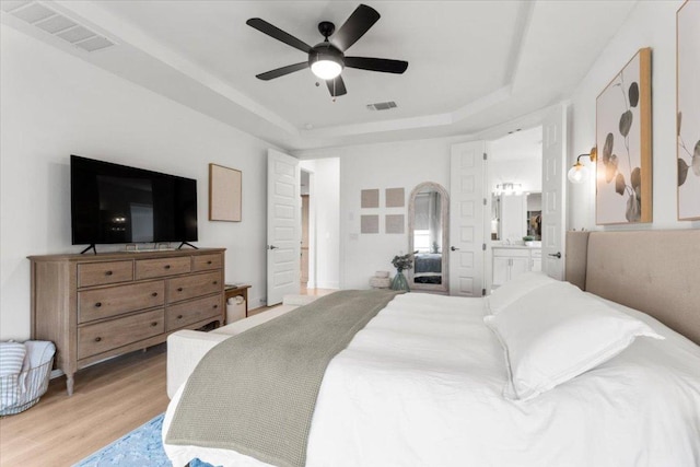 7913 Edmondson Bnd, Austin, TX 78744 - bedroom featuring a tray ceiling, light wood-style floors, connected bathroom, and a ceiling fan