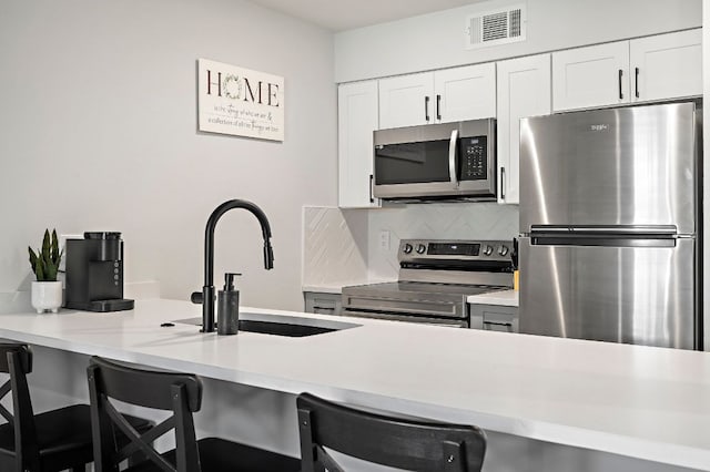 1203 Hollow Creek Dr Unit 101, Austin, TX 78704 - kitchen featuring appliances with stainless steel finishes, a kitchen bar, decorative backsplash, light countertops, and white cabinetry