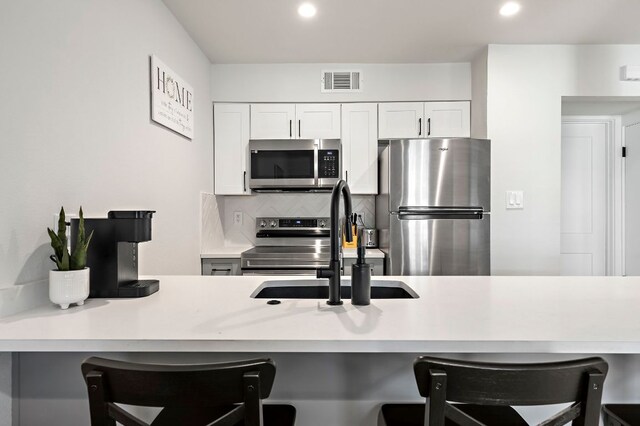 1203 Hollow Creek Dr Unit 101, Austin, TX 78704 - kitchen with appliances with stainless steel finishes, a kitchen bar, backsplash, light countertops, and white cabinets
