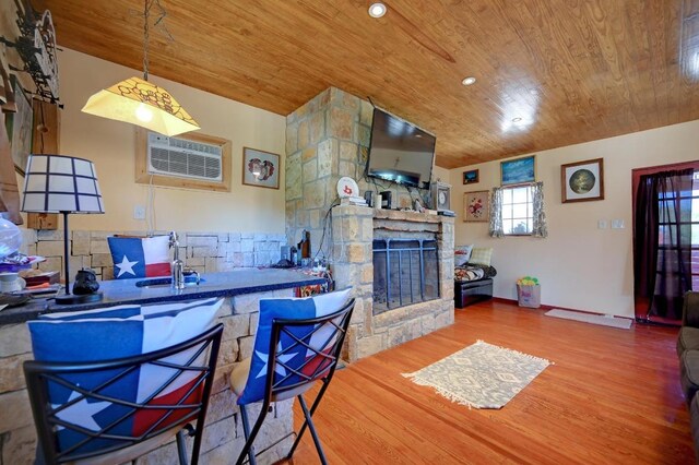 kitchen with wood finished floors, a stone fireplace, wood ceiling, a wall mounted AC, and hanging light fixtures