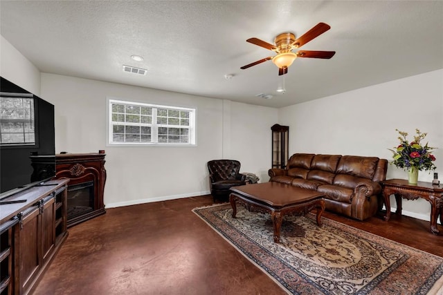 living area featuring finished concrete flooring, visible vents, baseboards, a glass covered fireplace, and a ceiling fan