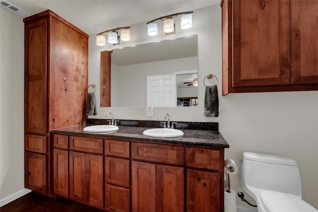 bathroom featuring toilet, double vanity, a sink, and visible vents
