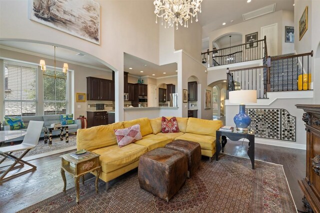 living room featuring crown molding, arched walkways, a towering ceiling, a notable chandelier, and dark wood-style floors