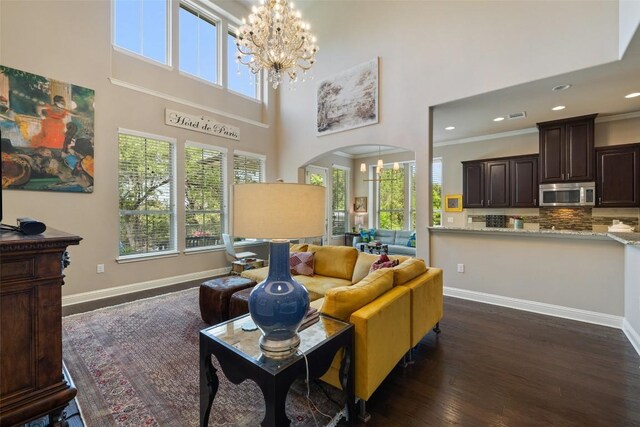living area featuring dark wood-style floors, arched walkways, a towering ceiling, baseboards, and a notable chandelier
