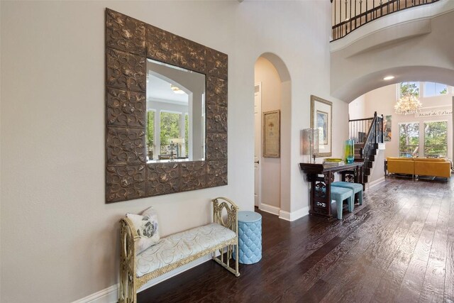 hallway featuring a towering ceiling, baseboards, wood finished floors, and arched walkways