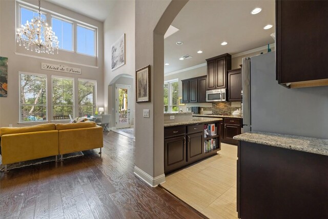 kitchen with dark brown cabinets, arched walkways, stainless steel microwave, a chandelier, and open floor plan