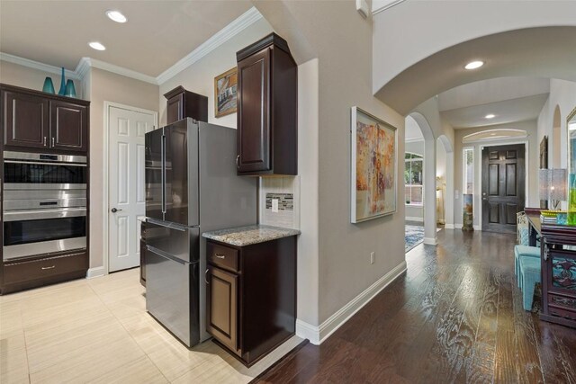 kitchen with stainless steel appliances, light stone counters, arched walkways, baseboards, and dark brown cabinetry