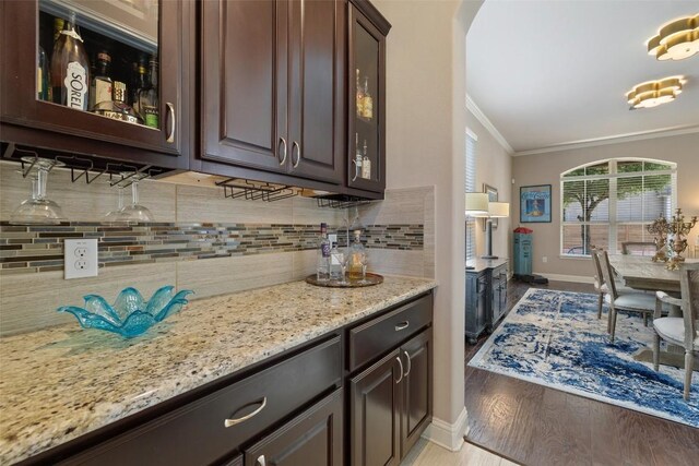 bar featuring light wood finished floors, arched walkways, baseboards, decorative backsplash, and crown molding