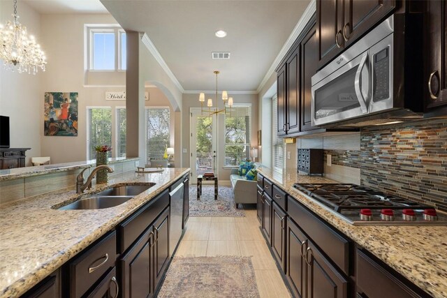 kitchen featuring a sink, stainless steel appliances, backsplash, a notable chandelier, and light stone countertops