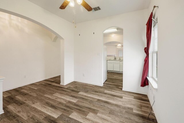 unfurnished room with a ceiling fan, wood finished floors, a sink, arched walkways, and visible vents