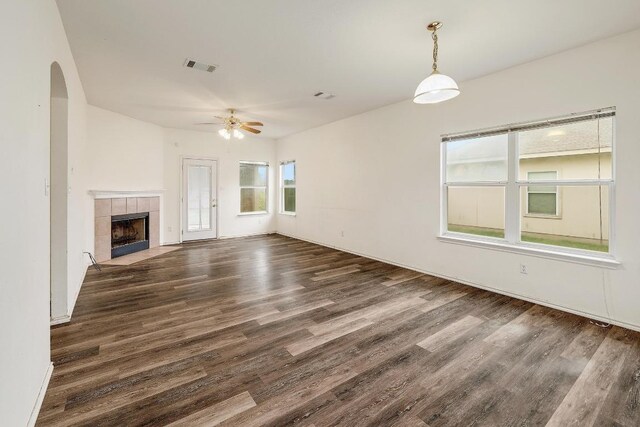 unfurnished living room with wood finished floors, ceiling fan, arched walkways, a fireplace, and visible vents