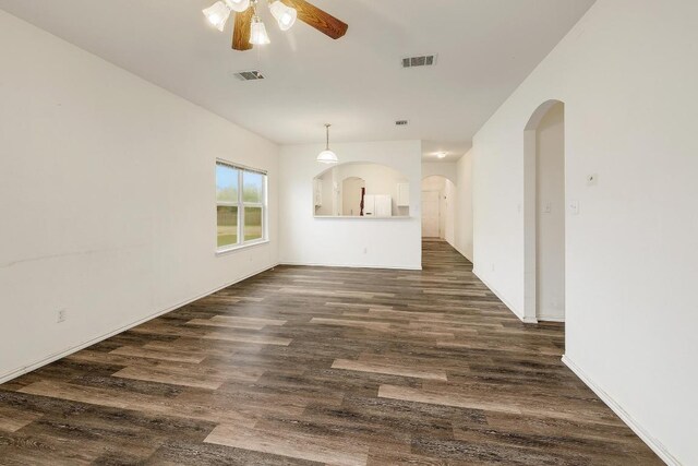 empty room with dark wood-type flooring, arched walkways, visible vents, and ceiling fan