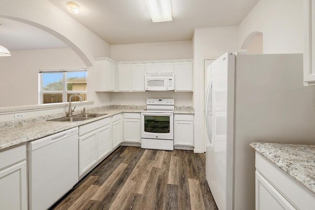 kitchen with white cabinets, dark wood finished floors, a sink, arched walkways, and white appliances