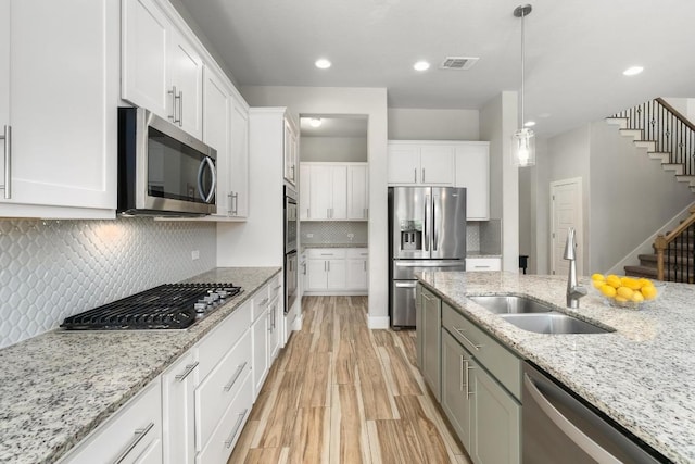 20401 Great Egret Ln, Pflugerville, TX 78660 - kitchen featuring stainless steel appliances, white cabinets, light wood-style flooring, hanging light fixtures, and tasteful backsplash