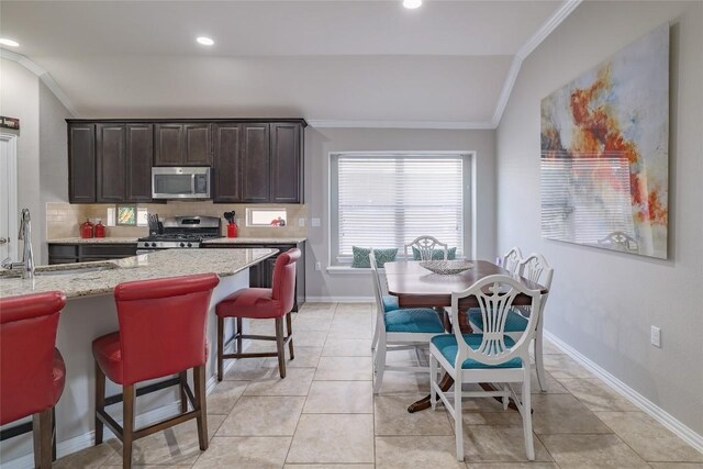 kitchen featuring lofted ceiling, a kitchen breakfast bar, a sink, crown molding, and appliances with stainless steel finishes