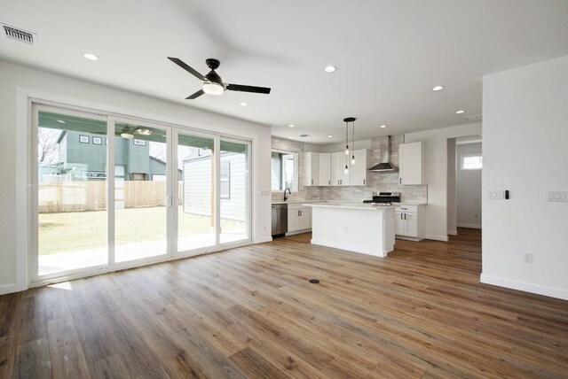 kitchen featuring stainless steel appliances, light countertops, wall chimney range hood, visible vents, and white cabinetry