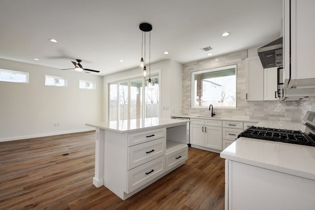 kitchen with wall chimney exhaust hood, a sink, range with gas cooktop, ceiling fan, and light countertops