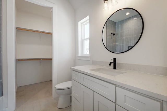 bathroom featuring a walk in closet, toilet, vanity, and tiled shower