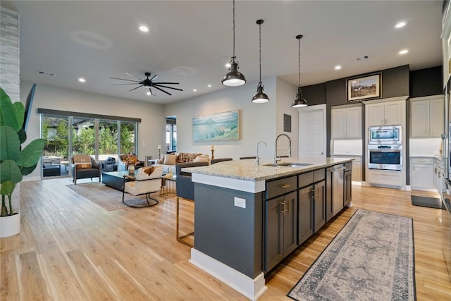 2500 Yuma Trl, Leander, TX 78641 - kitchen with appliances with stainless steel finishes, a kitchen island with sink, open floor plan, light wood finished floors, and light stone counters