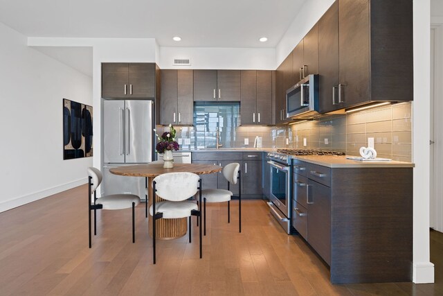 kitchen with dark brown cabinetry, visible vents, premium appliances, and light wood finished floors