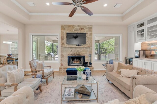 living area featuring wine cooler, visible vents, a ceiling fan, a stone fireplace, and a raised ceiling