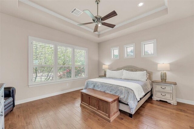 bedroom featuring crown molding, a raised ceiling, wood-type flooring, baseboards, and visible vents