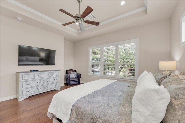 bedroom featuring crown molding, wood finished floors, a raised ceiling, baseboards, and visible vents