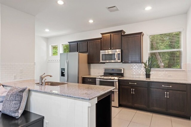 kitchen featuring dark brown cabinets, appliances with stainless steel finishes, light stone counters, a sink, and visible vents