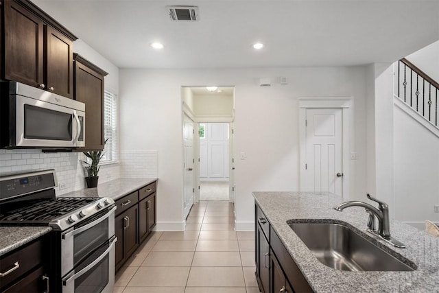 kitchen featuring dark brown cabinetry, visible vents, appliances with stainless steel finishes, light stone countertops, and a sink