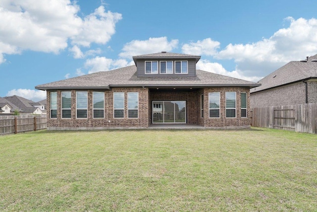 rear view of property with a fenced backyard, brick siding, a yard, and roof with shingles