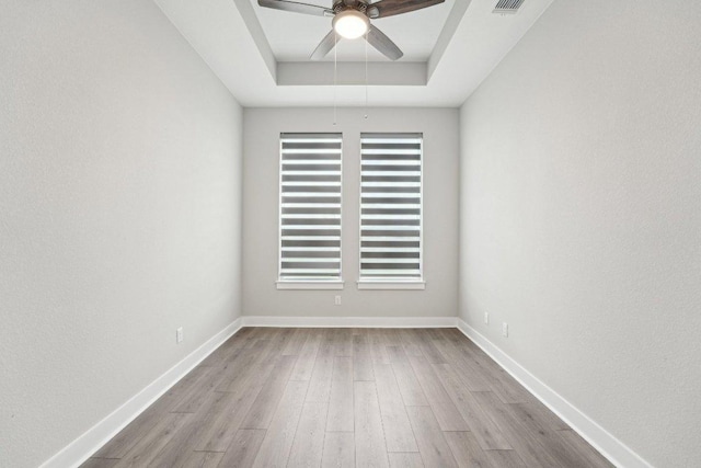 unfurnished room with ceiling fan, baseboards, wood finished floors, and a raised ceiling