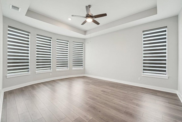 empty room with a raised ceiling, visible vents, baseboards, and ceiling fan