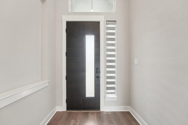 foyer featuring a textured wall, baseboards, and dark wood-type flooring