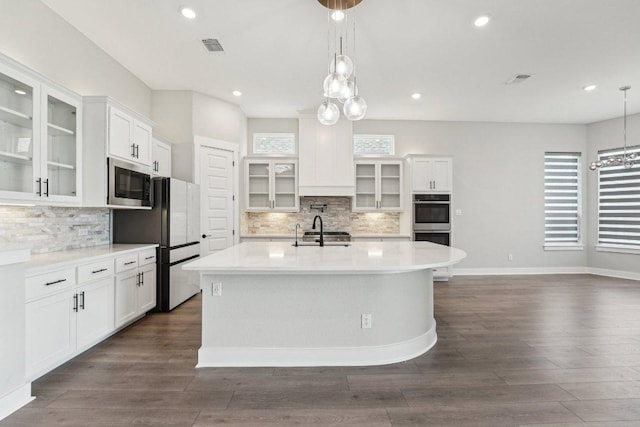 kitchen with a kitchen island with sink, light countertops, backsplash, and appliances with stainless steel finishes