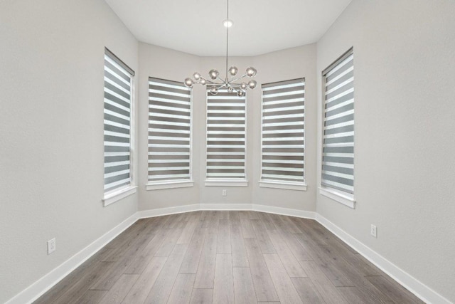unfurnished dining area with an inviting chandelier, wood finished floors, and plenty of natural light