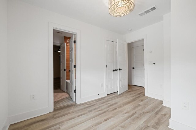 unfurnished bedroom featuring light wood-style floors, visible vents, baseboards, and ensuite bathroom