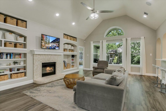 living area with high vaulted ceiling, a ceiling fan, wood finished floors, a fireplace, and visible vents