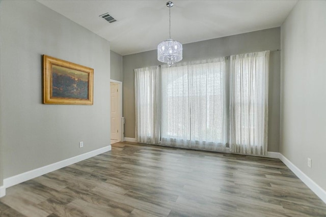 unfurnished dining area featuring a chandelier, wood finished floors, visible vents, and baseboards