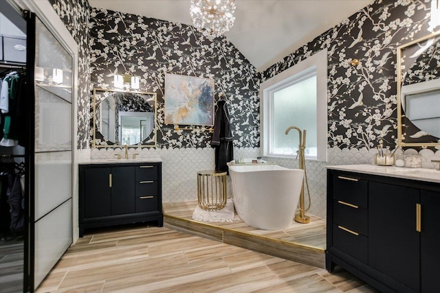 full bathroom featuring two vanities, a sink, vaulted ceiling, wallpapered walls, and a freestanding tub