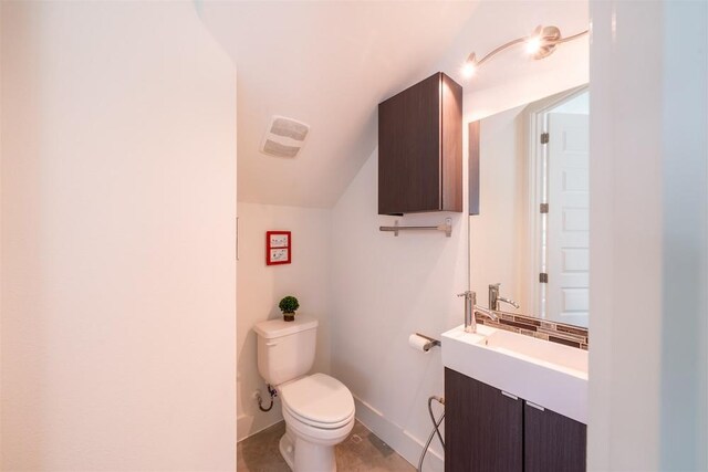 half bathroom featuring baseboards, vaulted ceiling, vanity, and toilet