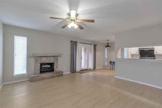 unfurnished living room featuring baseboards, a ceiling fan, light wood-style flooring, and a fireplace