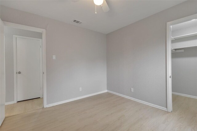 unfurnished bedroom featuring visible vents, baseboards, wood finished floors, ceiling fan, and a walk in closet