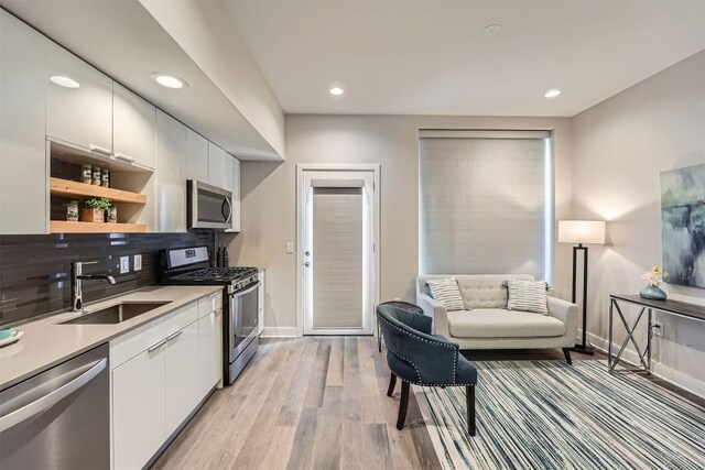 kitchen with a sink, light wood-type flooring, stainless steel appliances, white cabinets, and baseboards