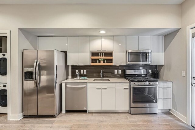 kitchen featuring decorative backsplash, appliances with stainless steel finishes, stacked washer and clothes dryer, and white cabinetry
