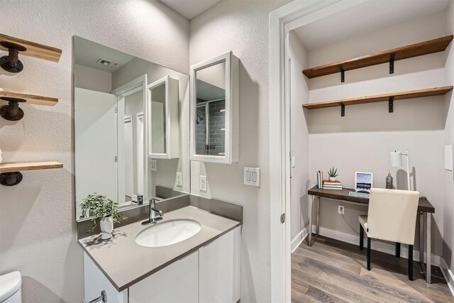 bathroom with wood finished floors, toilet, vanity, and a textured wall