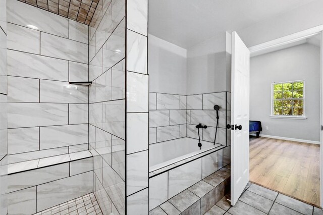 bathroom featuring wood finished floors, tiled tub, baseboards, and tiled shower