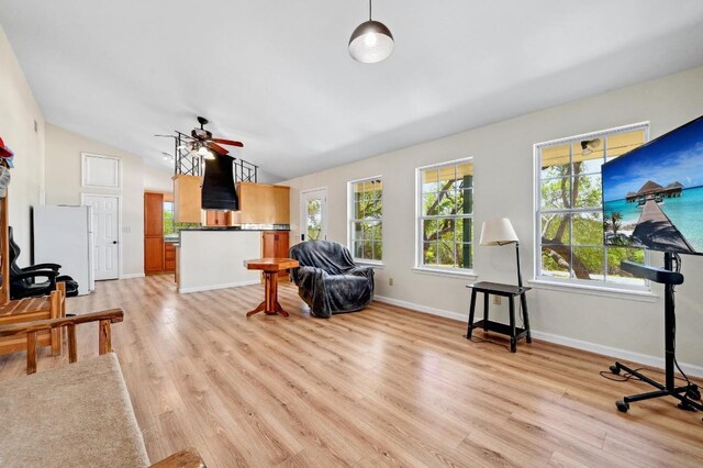 living area featuring light wood-style flooring, baseboards, vaulted ceiling, and a ceiling fan