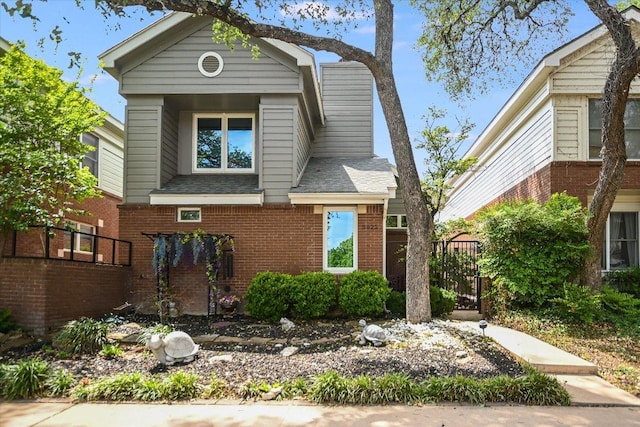 view of front of property featuring brick siding, roof with shingles, and fence